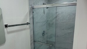 A bathroom with a glass-enclosed shower, a white toilet, and a sink with a wooden vanity. - Private studio in north Long Beach with refreshing AC (Long Beach)