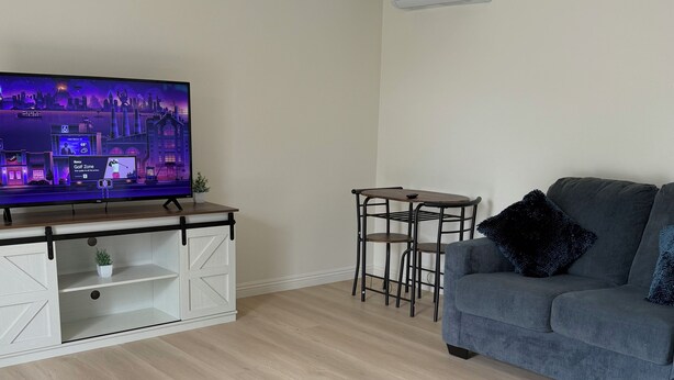 A living room with a flat-screen TV, a grey sofa, a small table, and a wooden floor. - Private studio in north Long Beach with refreshing AC (Long Beach)