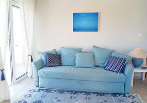 Ein hellblaues Sofa mit gemusterten Kissen, ein blaues Bild an der Wand, eine Lampe und ein Teppich mit Muster.