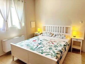 Ein Schlafzimmer mit einem Bett, zwei Nachttischen, einem Heizkörper und einem Fenster mit Vorhängen.