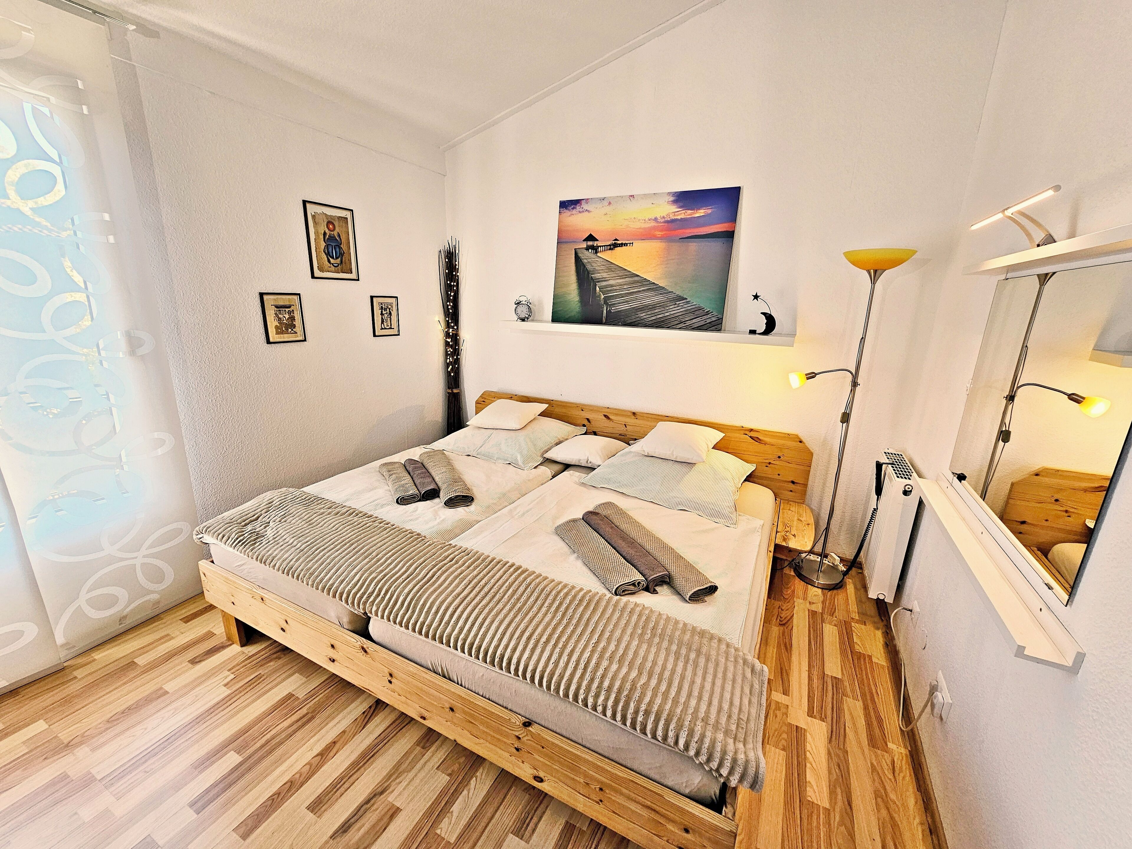 Een slaapkamer met een houten bed, een nachtkastje, een spiegel en een schilderij aan de muur.