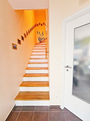 A staircase with wooden steps leading to a landing, a door with a glass panel, and a wall with framed pictures. - Vacation home / apartment in Koblenz with terrace (Koblenz)
