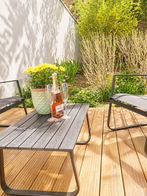 Une terrasse en bois avec une table dressée pour deux personnes, une bouteille de vin et un vase rempli de fleurs jaunes.