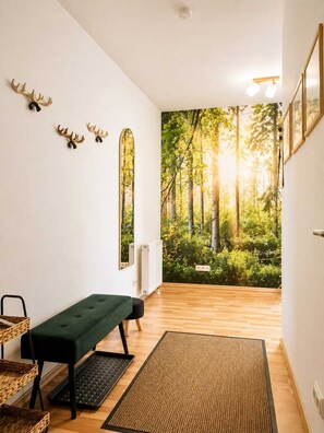 Une pièce avec un banc vert, un clavier, une chaise en osier, un radiateur et une fresque représentant une forêt sur le mur.