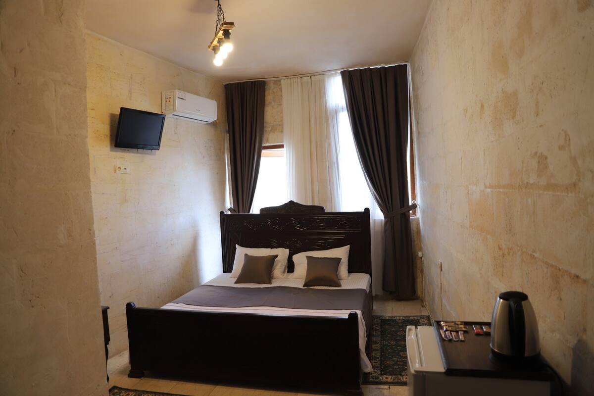 A hotel room with a bed, a television mounted on the wall, a coffee maker, and a window with curtains.