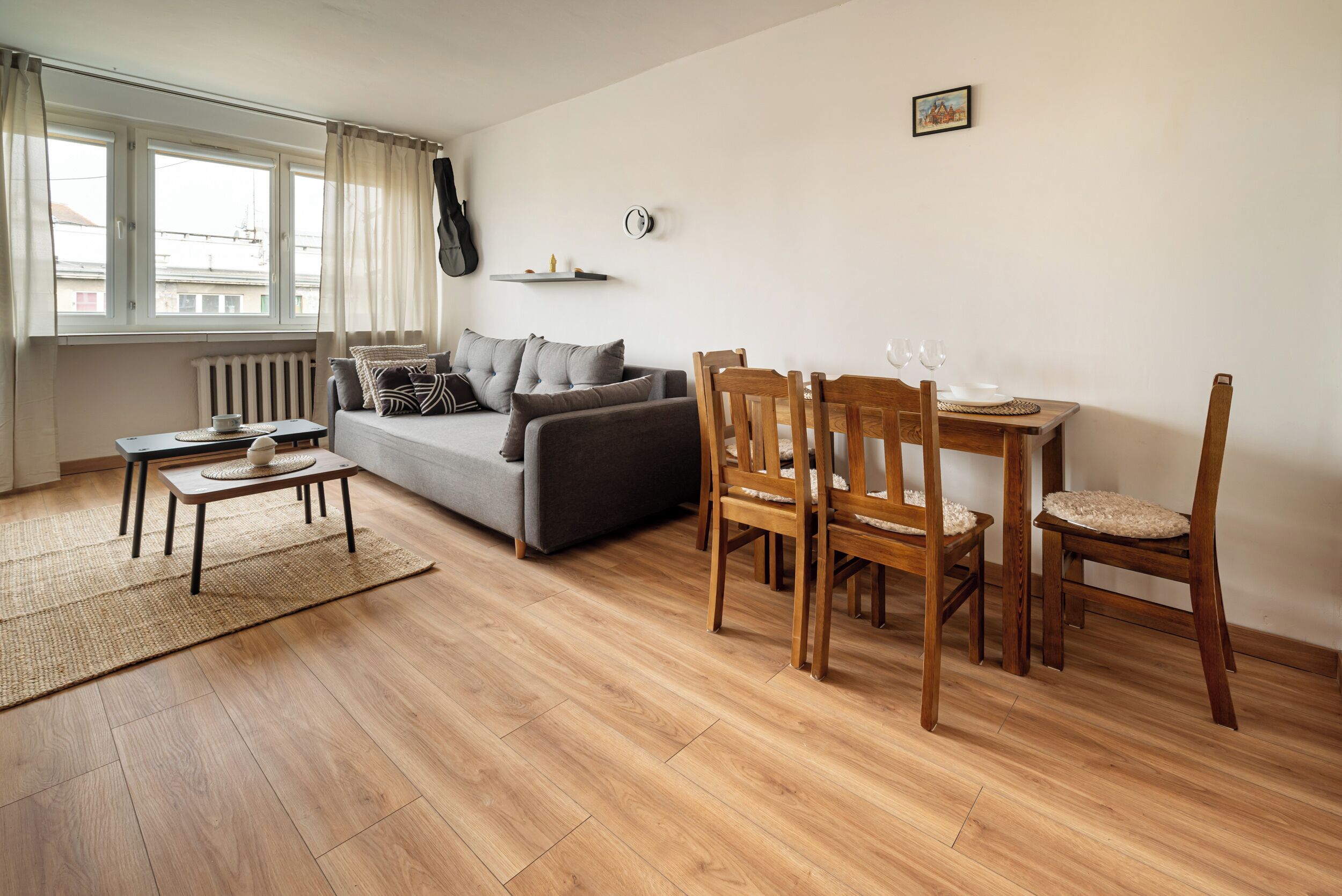 A living room with a sofa, wooden chairs, a small table, and a dining table with chairs.