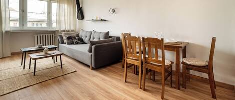 A living room with a sofa, wooden chairs, a small table, and a dining table with chairs.