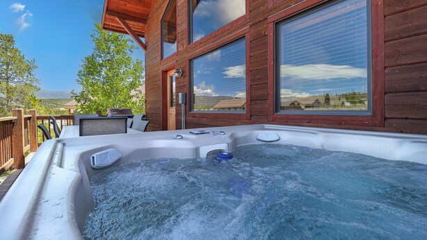 Een houten blokhut met een hottub, grote ramen en een terras.