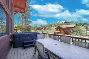 A wooden deck with a hot tub and table, overlooking a residential area with houses and trees.