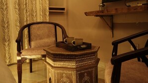 A room with a wooden chair, a small table with a tray, and a shelf against the wall. - Stay Stories (Chopra)