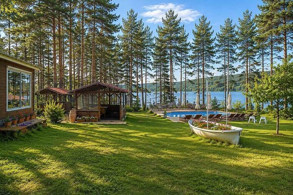A cabin with a deck, a swimming pool, and a view of a lake surrounded by trees.