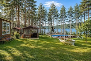 A cabin with a deck, a swimming pool, and a view of a lake surrounded by trees.