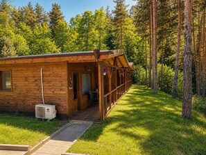 Una cabaña de madera con un porche, un ventanal pequeño y una puerta con un letrero de 'Welcome'.