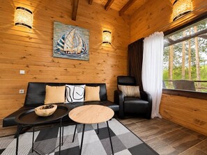 A wooden interior with a sofa, a chair, a round table, and a painting of a sailboat.