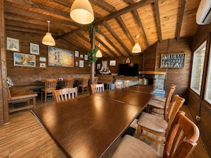 A rustic wooden interior with a long dining table, wooden chairs, pendant lights, and nautical-themed artwork.