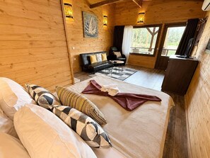 A wooden cabin with a bed, a sofa, a dining area, and a view of the outdoors.