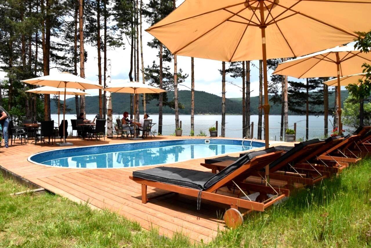 A swimming pool with lounge chairs and umbrellas, surrounded by a wooden deck and trees.