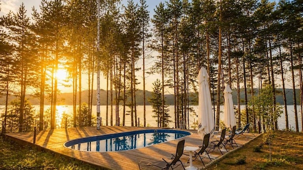 A wooden deck with a pool, surrounded by tall trees and overlooking a body of water. - Club Paradise Bay Iskar Lake (Sofia)