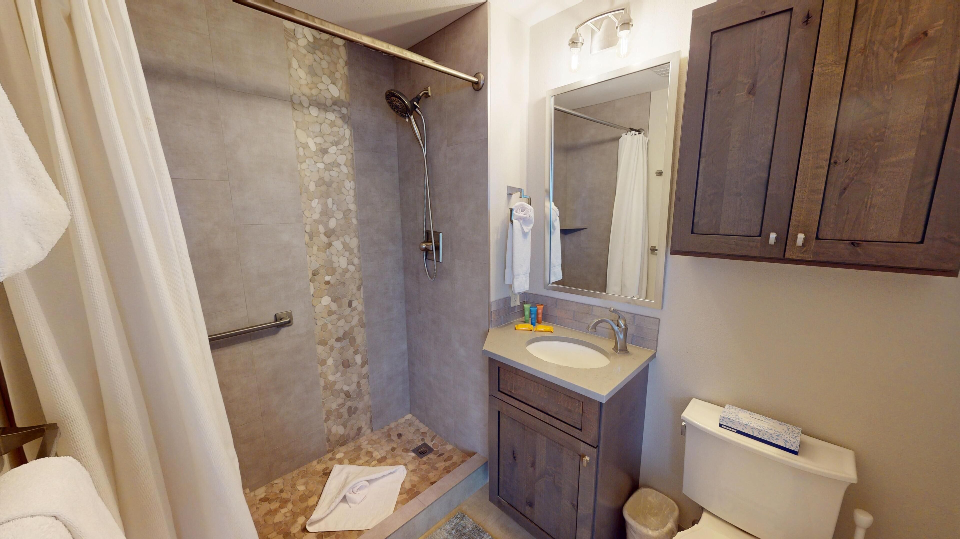 A bathroom with a shower, toilet, sink, and mirror.