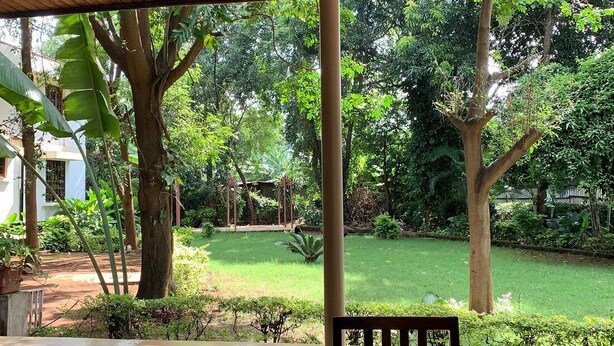 A covered outdoor seating area with a view of a garden and trees. - kilimanjaro safari lodge (Moshi)