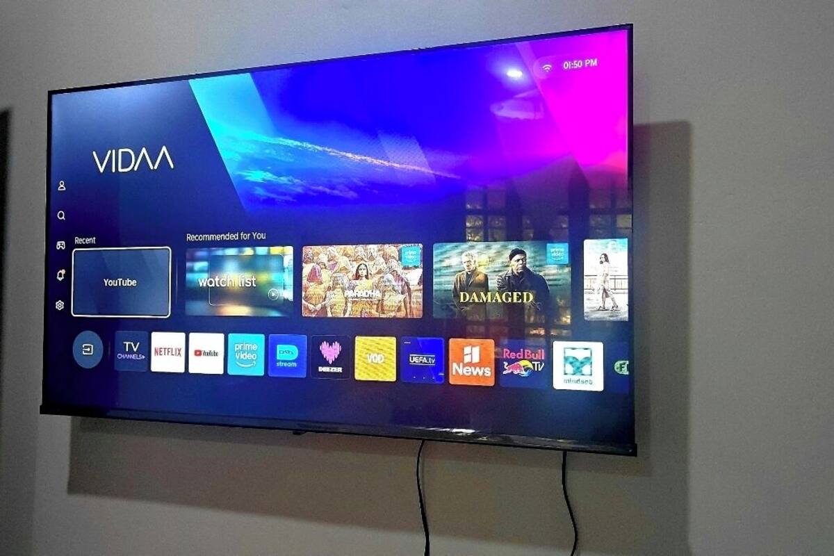 A flat-screen TV mounted on a wall displaying a user interface with various streaming service icons and a YouTube search bar.