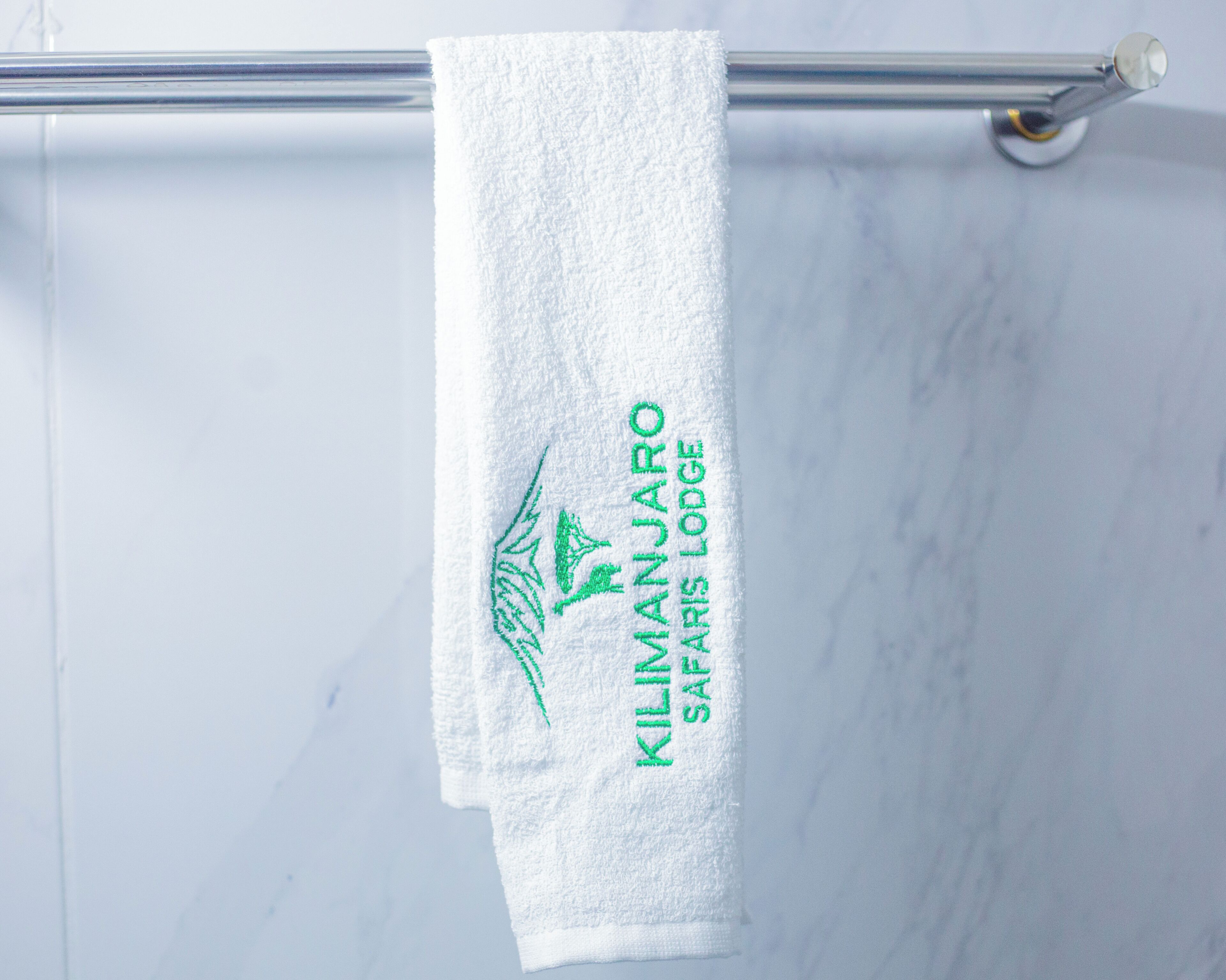 Een witte handdoek hangend aan een metalen handdoekhouder met groene tekst en een bladlogo.