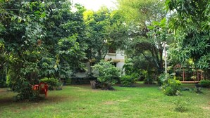 A lush garden with a swing set, a red chair, and a building in the background. - kilimanjaro safari lodge (Moshi)