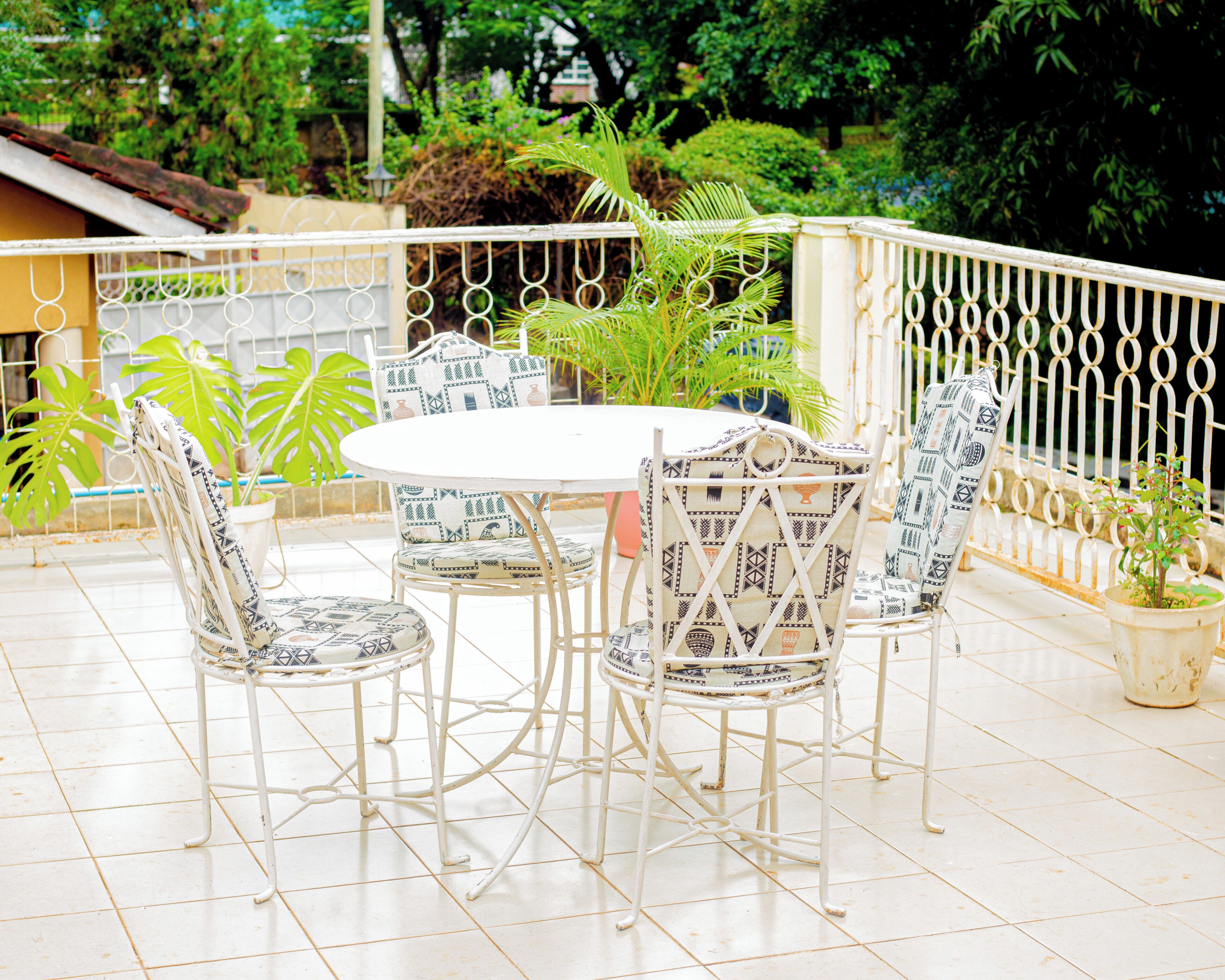 A white metal table and chairs with patterned cushions, surrounded by potted plants and a white railing.