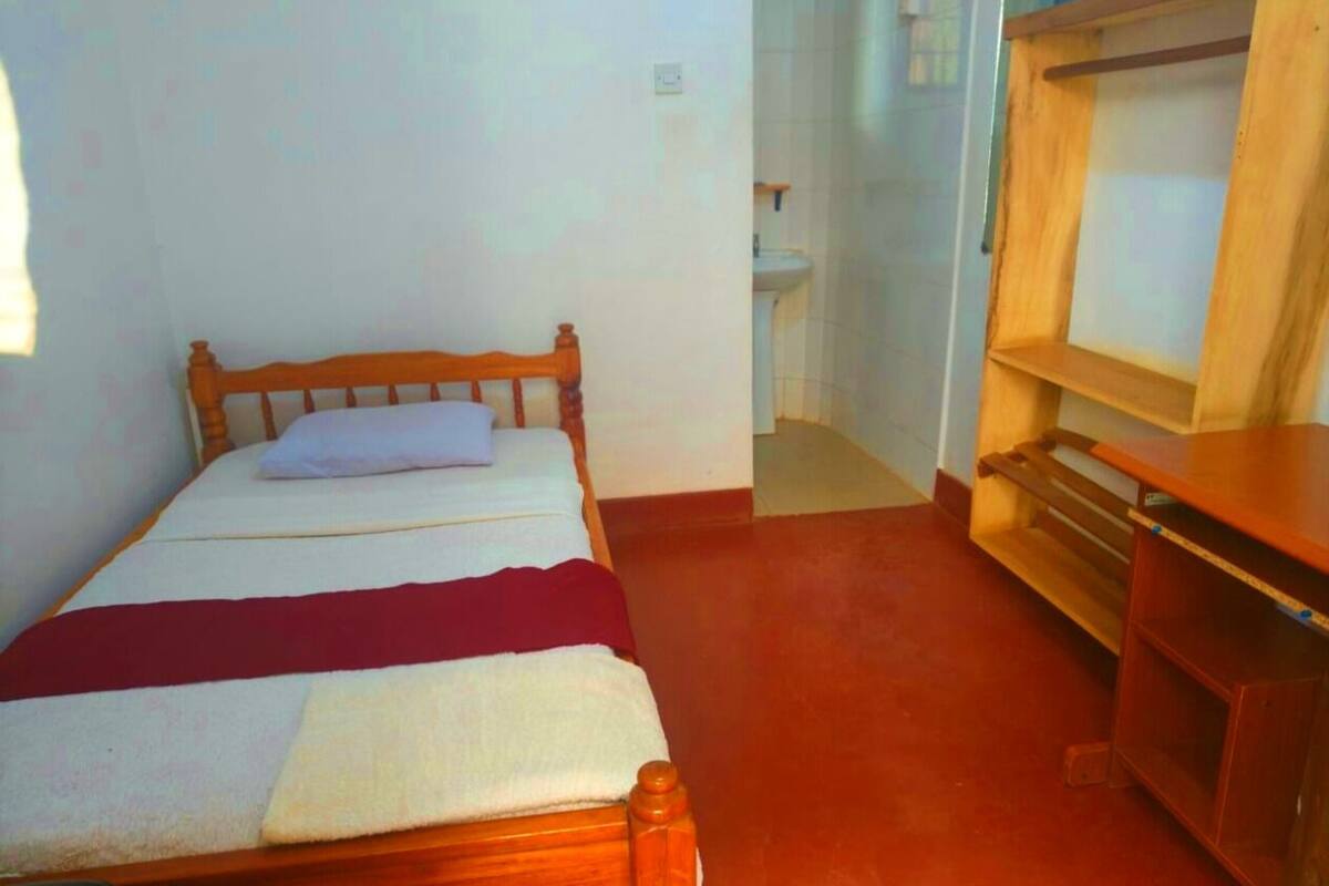 A single bed with a wooden headboard, a bedside table, and a wooden bench.