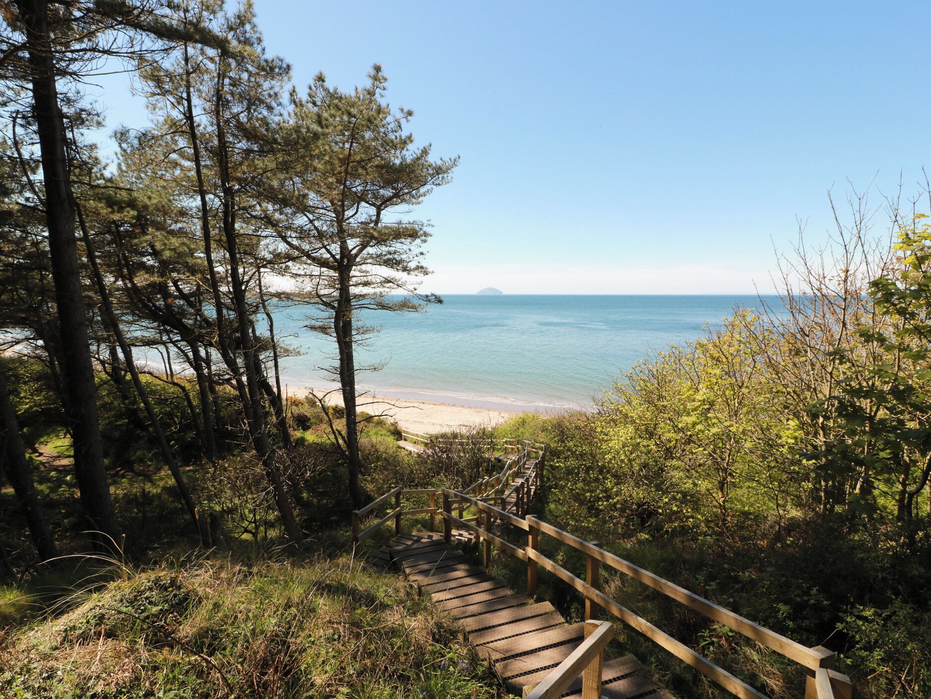 Eine Holztreppe führt zu einem Strand mit freiem Blick auf das Meer und eine entfernte Insel.