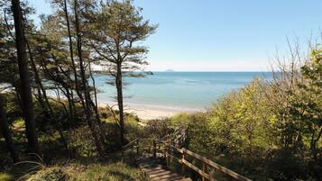 Eine Holztreppe führt zu einem Strand mit freiem Blick auf das Meer und eine entfernte Insel.