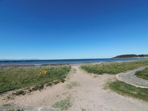 Un sentier côtier menant à une plage, avec un ciel dégagé.
