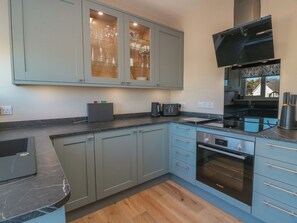 A modern kitchen with grey cabinets, a Bosch oven, and a black range hood. - Castaway Cottage Maidens (Girvan)