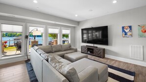 A modern living room with a sectional sofa, a flat-screen TV, and large windows overlooking a pool. - Kiser Island (Terrell)
