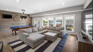 A modern living room with a pool table, a sectional sofa, and large windows. - Kiser Island (Terrell)