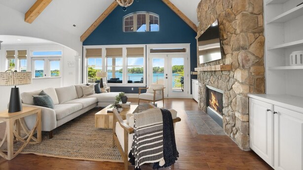A spacious living room with a stone fireplace, large windows, and a high ceiling with exposed beams. - Kiser Island (Terrell)