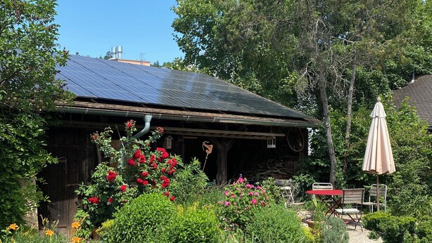 Una construcción rústica con techo de paneles solares, rodeada por un jardín con diversas plantas y flores.