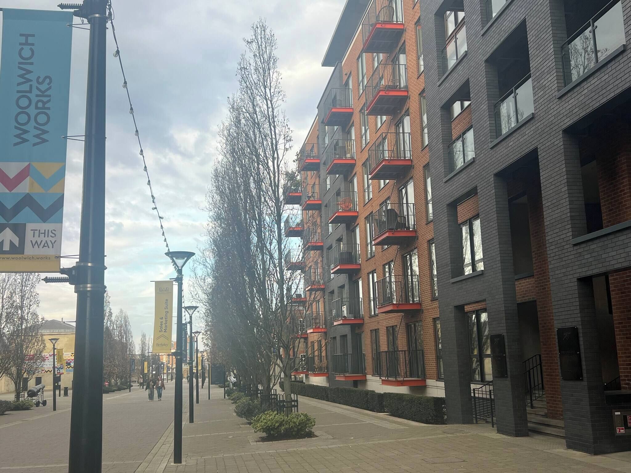 A modern urban street with multi-story buildings, a clear sky, and a pedestrian pathway.
