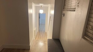 A narrow hallway with a bench, a light fixture, and a door leading to another room.