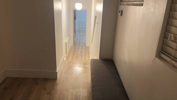 A narrow hallway with a bench, a light fixture, and a door leading to another room.