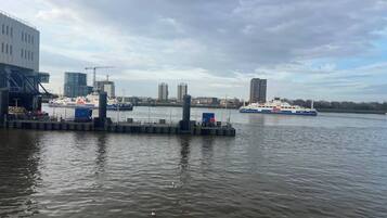 A waterfront dock with a ferry, a building with a crane, and several high-rise buildings in the background.