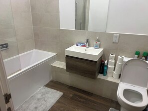 A bathroom with a bathtub, a sink with toiletries, a toilet, and a mirror. - Cosy 1bed Perfect for Family and Contractors (London)