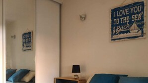 Un dormitorio con cama, mesita de noche, lámpara, espejo y una pared decorada con un cartel.
