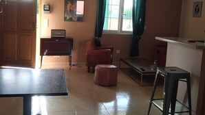 Una sala de estar con una mesa de comedor, un sofá, un pequeño otoman, un televisor y un ventilador de techo.