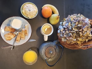A breakfast setting with toast, a bowl of cereal, a cup of coffee, a fruit bowl, a teapot, and a decorative plant.
