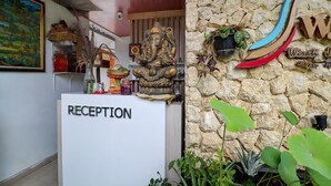 A reception desk labeled 'RECEPTION' with a statue of an elephant deity, a stone wall, and a sign that reads 'Wristi Guest House.'