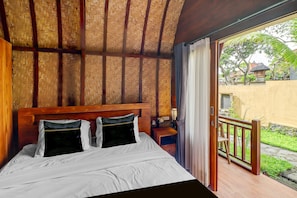 A room with a bed, wooden headboard, and a view of a garden through an open door. - Hotel O near Mookiland Park Bali formerl (Kerobokan)