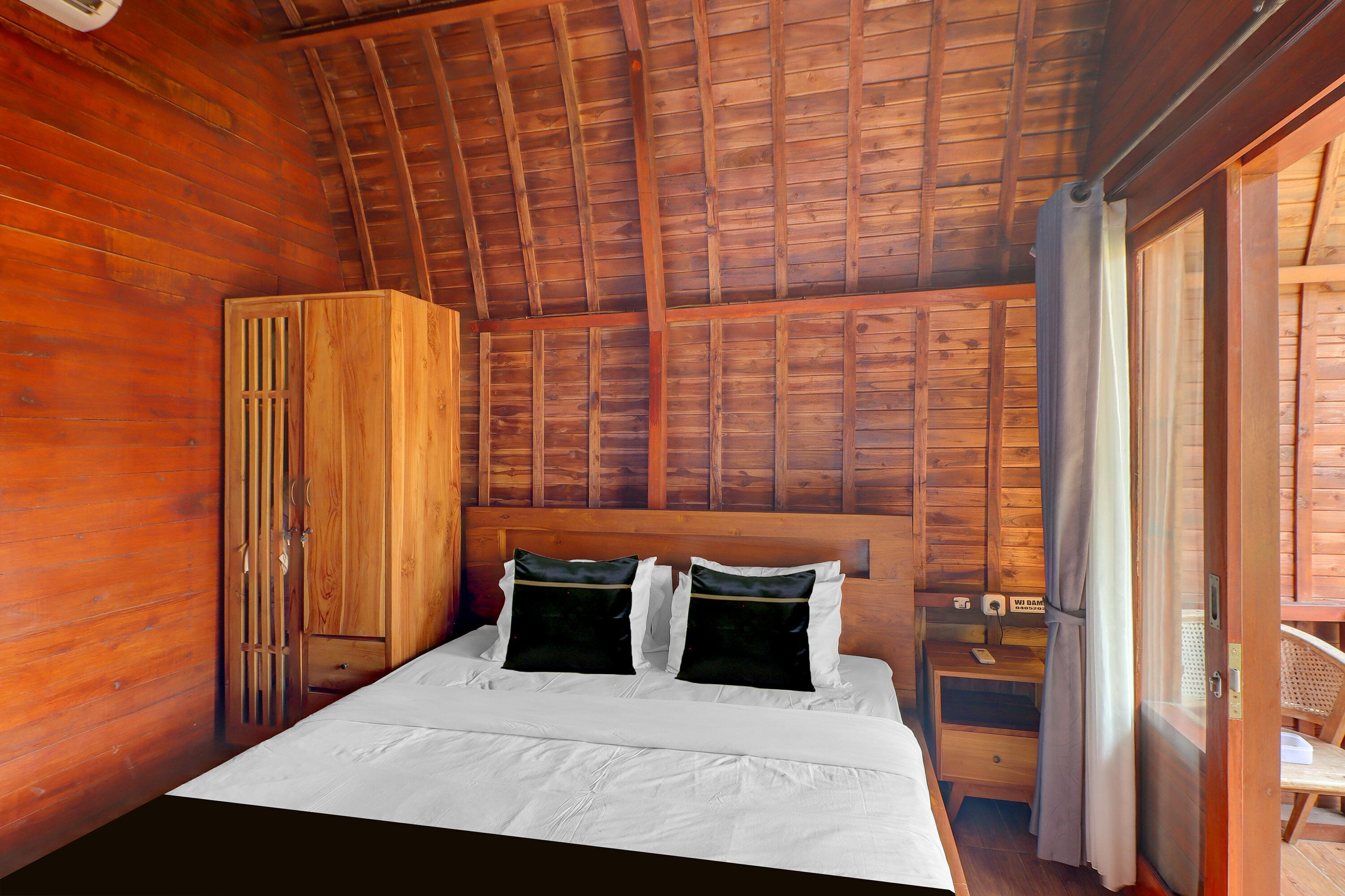 A wooden cabin bedroom with a bed, a wardrobe, and a small table with a chair.