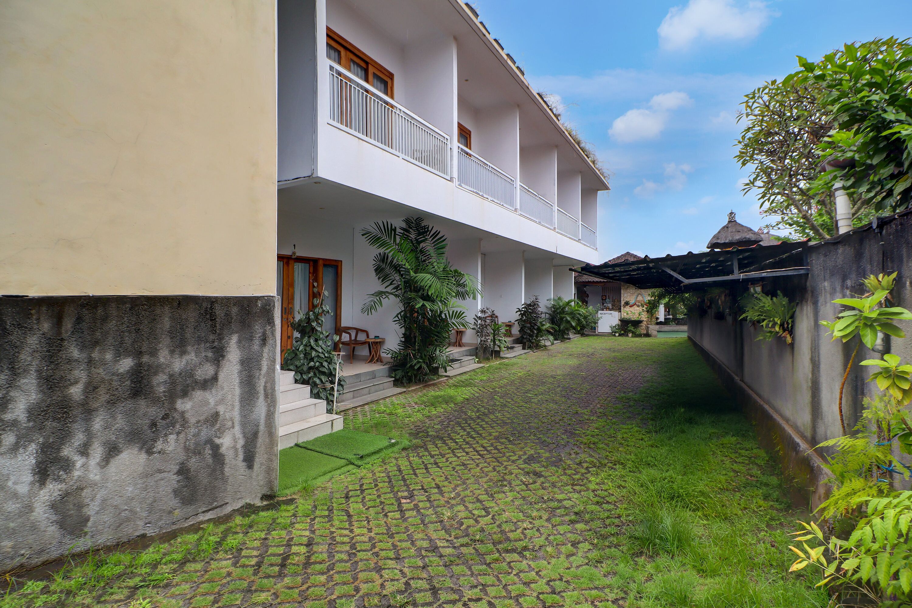 A two-story building with a covered balcony, a paved courtyard, and a small water feature.