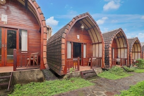 A row of wooden cabins with arched roofs, wooden railings, and a stone pathway leading to the entrance. - Hotel O near Mookiland Park Bali formerl (Kerobokan)